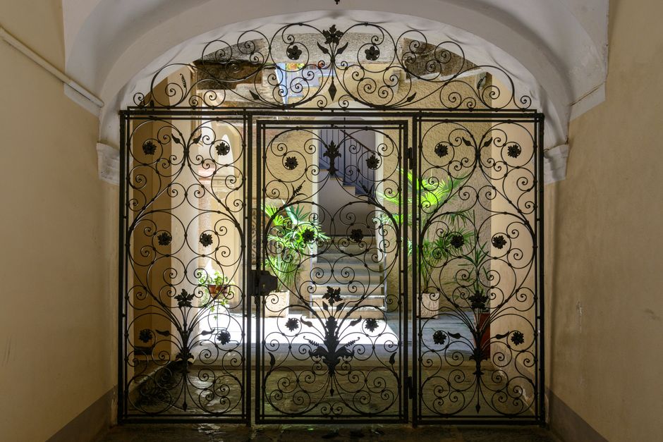 Elegant iron gate with intricate designs opening into a sunlit corridor with plants.